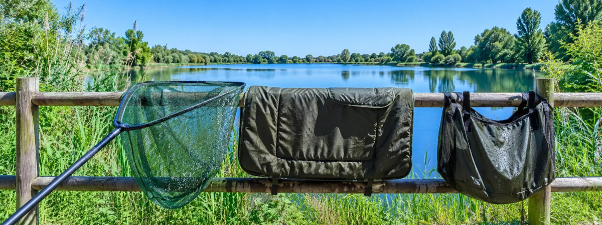 Une épuisette, un tapis de réception et un sac de pesée qui sèchent au soleil sur une barrière en bois, au bord d'un étang.