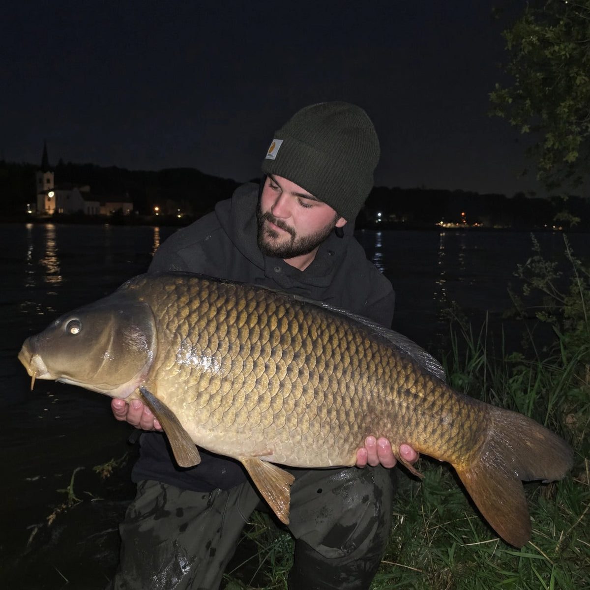 Carpe commune prise de nuit sur la Seine, avec les lumières d'un village sur l'autre rive