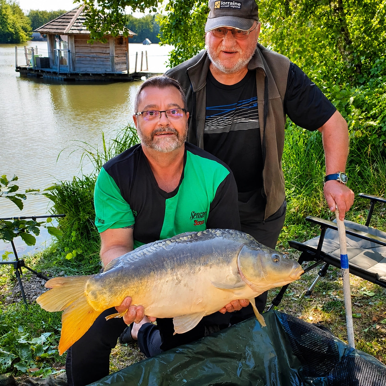 Deux pêcheurs avec une carpe miroir devant une cabane flottante de l'étang du Domaine de la Dombes