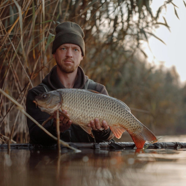 Carpiste en bonnet présentant une carpe commune aux écailles régulières en bord d'étang