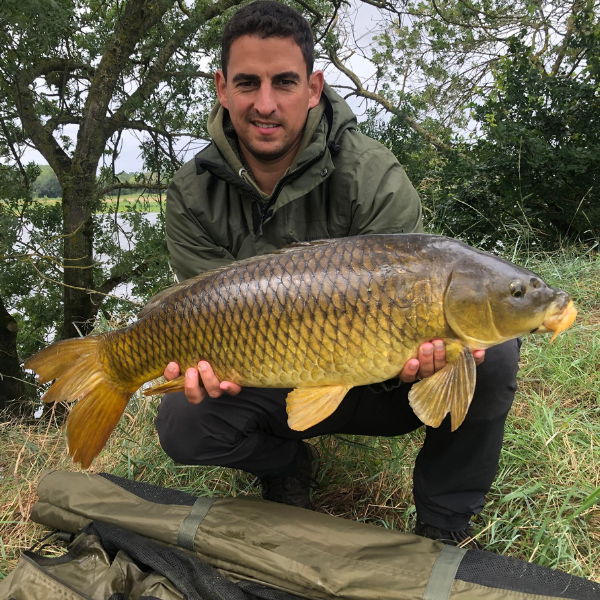 Pêcheur accroupi tenant une grande carpe commune à l'écaillure complète et régulière, belle prise lors d'une session de pêche à la carpe en France
