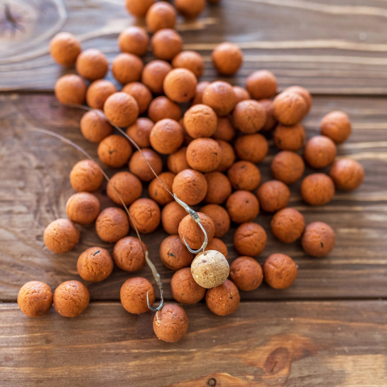 Bas de ligne et hameçons à œillet posés au milieu de bouillettes sur une table en bois