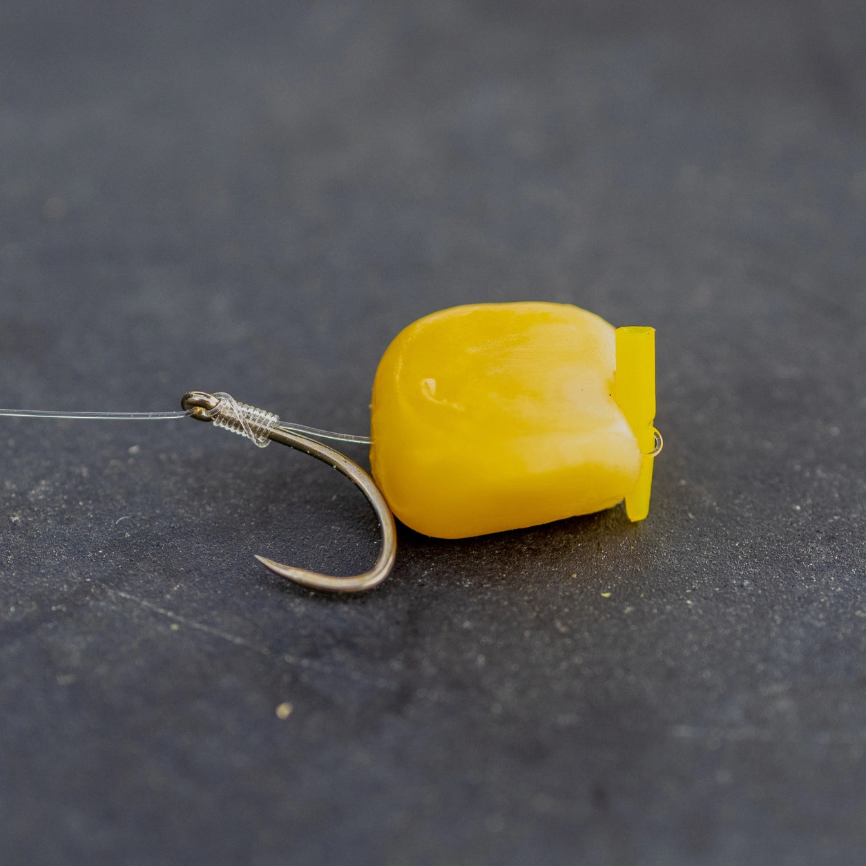 Hameçon ligaturé avec un grain de maïs artificiel jaune sur fond d'ardoise