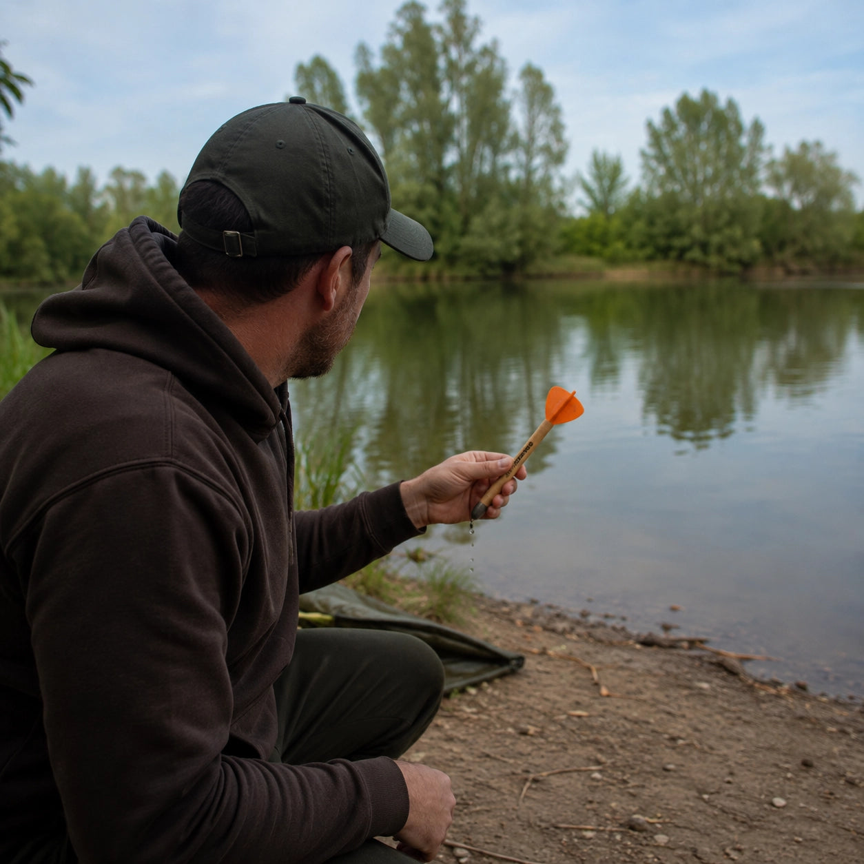 Carpiste accroupi au bord d'un lac, tenant un marker dans sa main