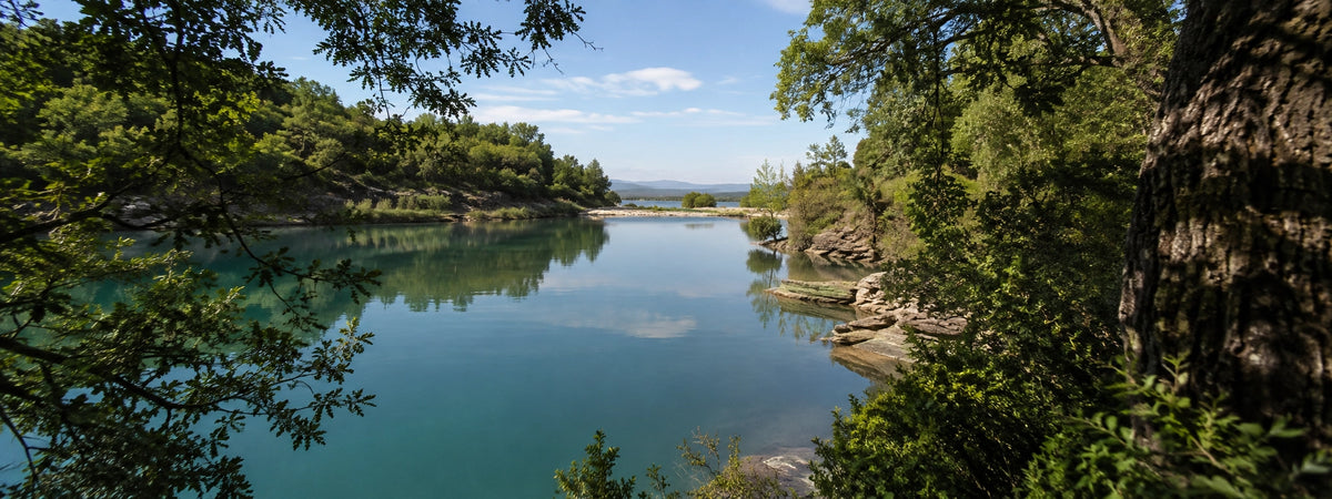 Plan d'eau aux reflets turquoise bordé de chênes et de rochers dans le Gard