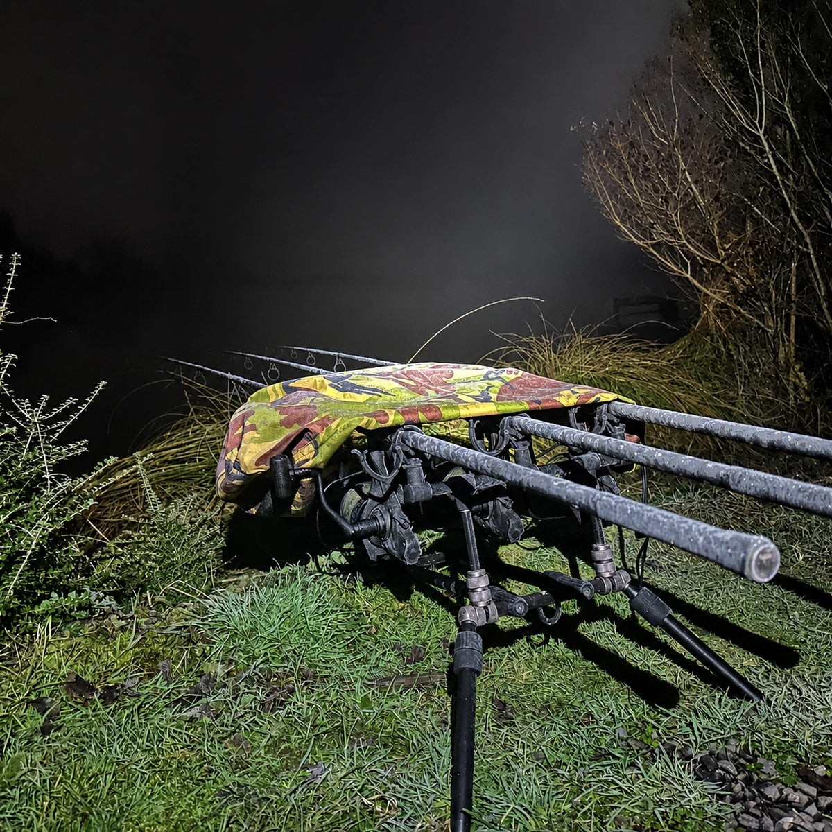 Rod pod protégé d'une housse camo posé de nuit au bord de la berge