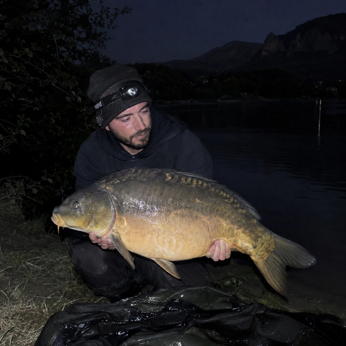 Carpiste de nuit dans l'Ariège présentant une carpe miroir au bord d'un lac