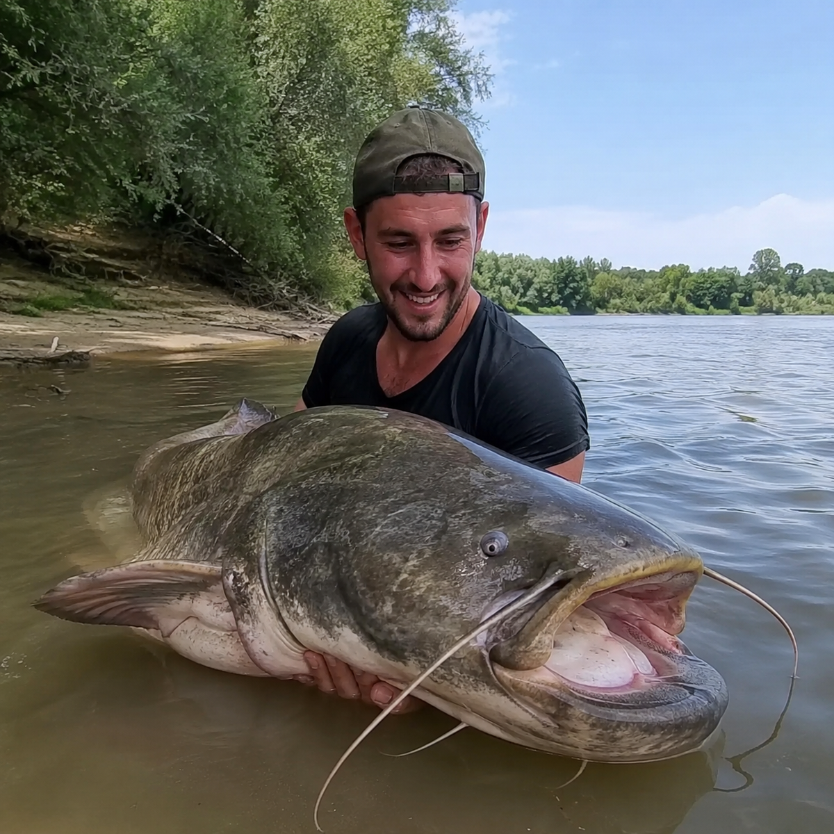 Pêcheur avec un gros silure sur une berge de sable dans le Gers